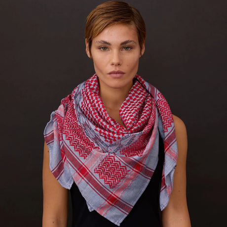Front view portrait of short-haired model wearing SEP blue and red keffiyeh scarf layered around her neck against a dark background