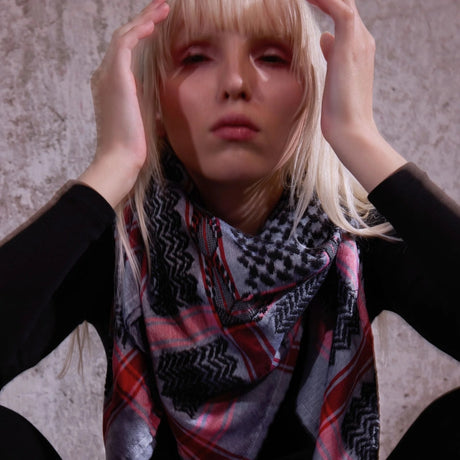 Close-up portrait of blonde model wearing SEP grey and black keffiyeh scarf styled around her neck over black clothing