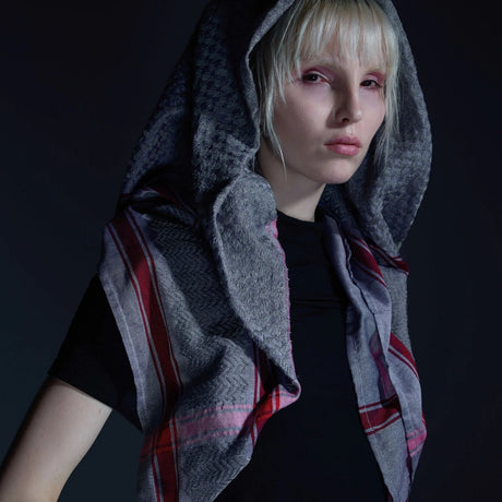 Dramatic studio portrait of model wearing SEP grey thalia keffiyeh scarf styled over her head like a hood against a dark background