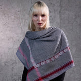 Blonde model wearing SEP grey thalia keffiyeh scarf draped over her shoulders as a wrap shawl against a concrete wall