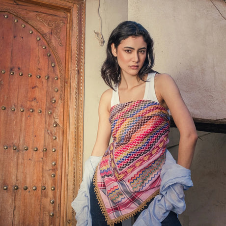 Model wearing SEP pink multicolor keffiyeh scarf styled as a strapless top standing near a wooden door
