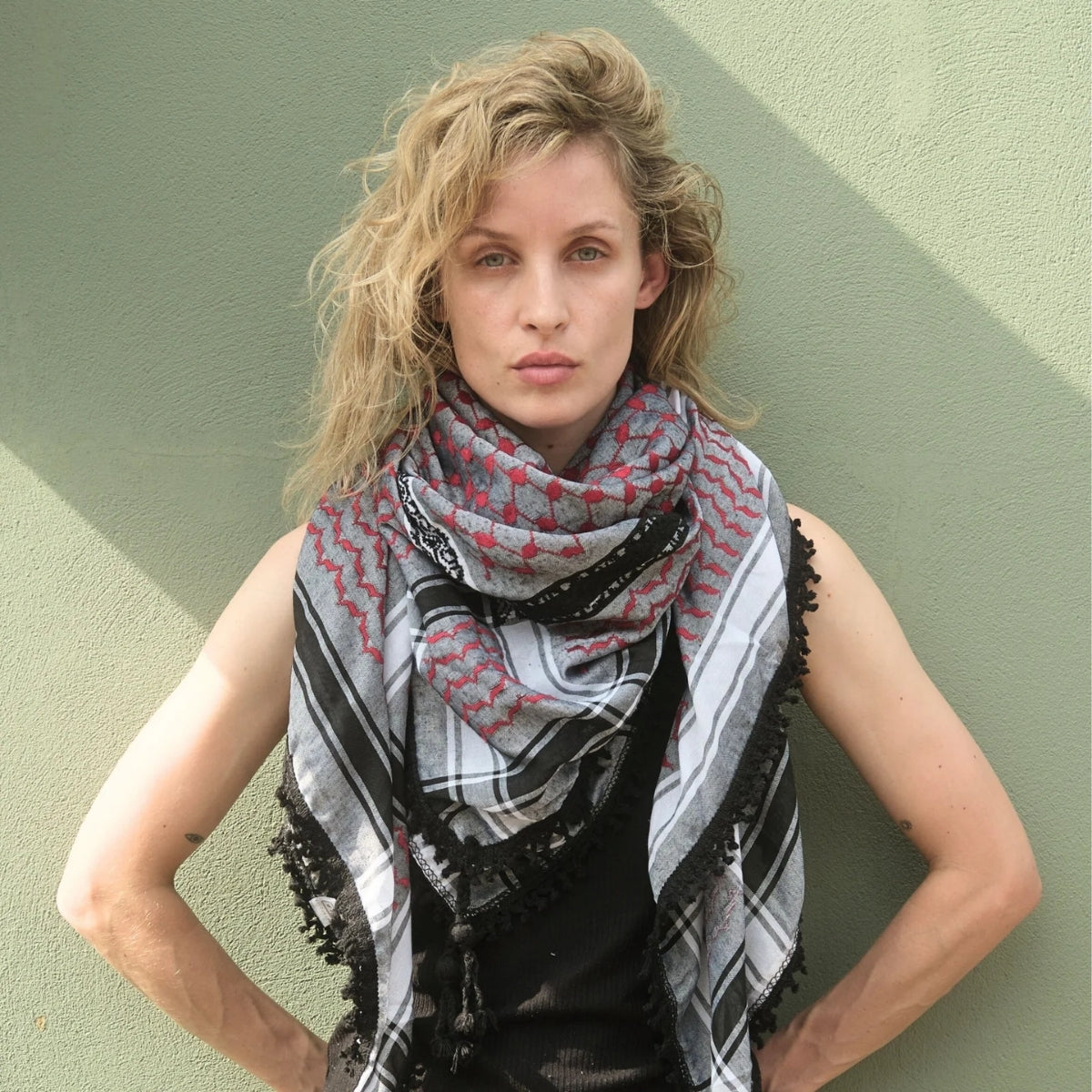Model wearing SEP red and grey keffiyeh scarf layered around her neck posing against a sage green background