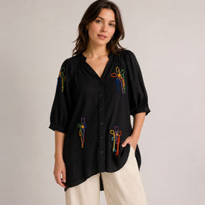 Woman wearing black embroidered shirt dress with balloon sleeves and button front, styled with wide leg trousers