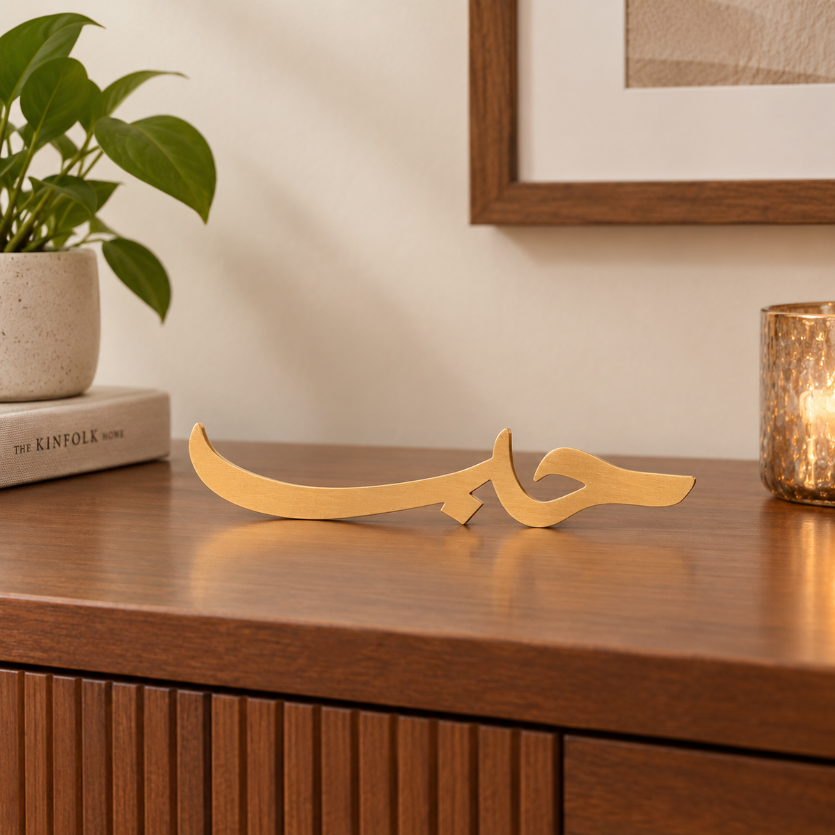 Tabletop view of the You & Eye Arabic Calligraphy Love copper metal decor displayed on a wooden credenza next to a potted plant and candle.