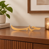 Tabletop view of the You & Eye Arabic Calligraphy Love copper metal decor displayed on a wooden credenza next to a potted plant and candle.