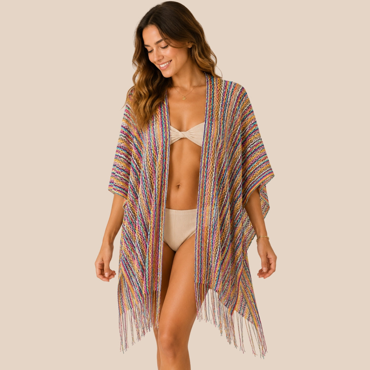 Front view of model wearing You & Eye rainbow fringe crochet short poncho with unstitched sides over a beige two-piece swimsuit